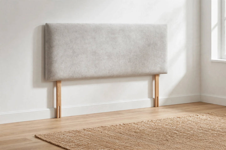 Plain light silver grey velvet headboard with oak strut legs standing against white bedroom wall on light oak wood floor with jute rug natural daylight - St James Beds