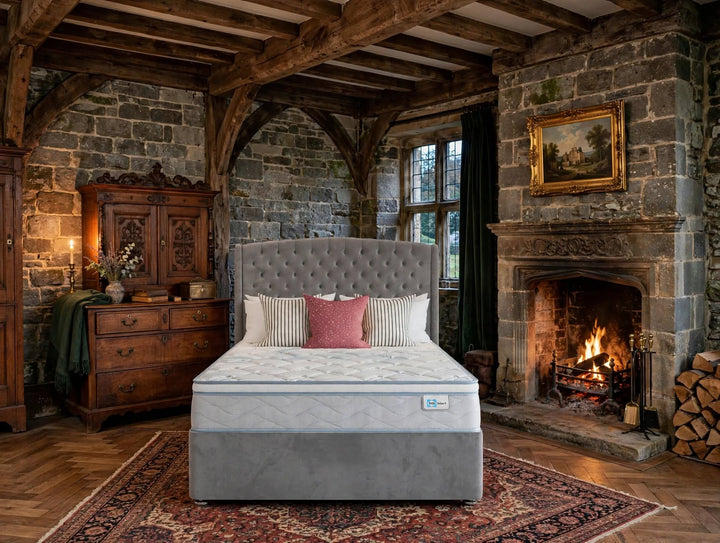 Sealy Burnham Select mattress and divan bed with grey buttoned headboard and striped pillows in old styled manor house bedroom with stone walls and fireplace